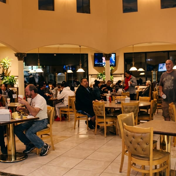 Busy restaurant interior with patrons dining at tables and booths under warm lighting.