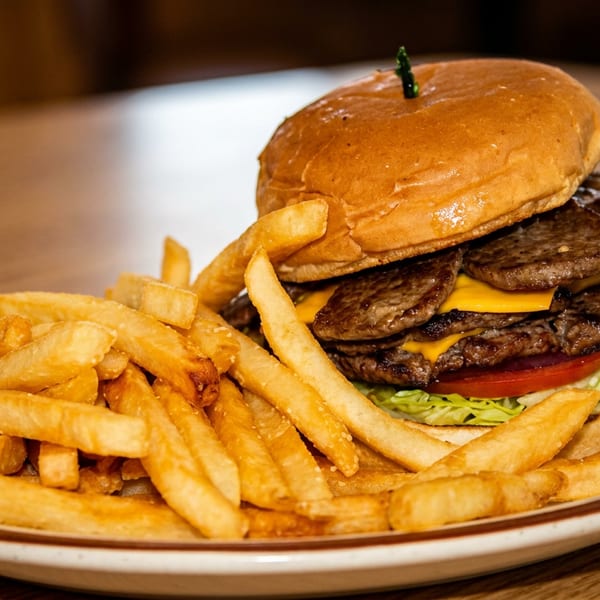 Double cheeseburger with lettuce, tomato, and golden french fries on a white plate.