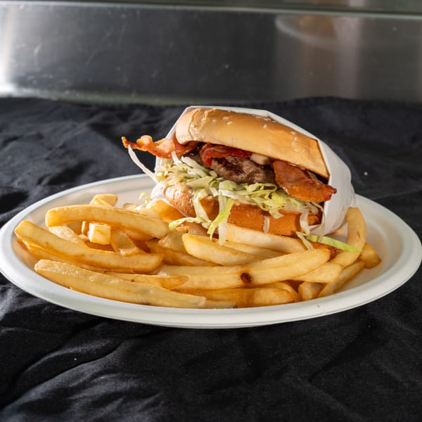 A bacon cheeseburger with lettuce and sauce, wrapped in paper, served with a side of fries.