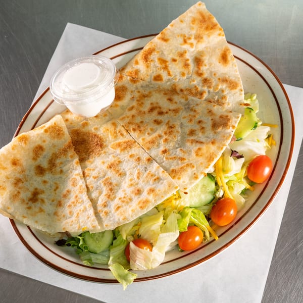 A quesadilla cut into four triangles, served on a bed of fresh salad with a side of sour cream.