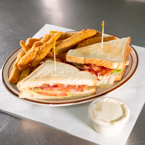 A plate with two club sandwich halves, golden fried pickles, and a side of dipping sauce.