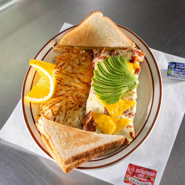 Breakfast plate with hash browns, omelet topped with avocado and cheese, toast, and orange slice.