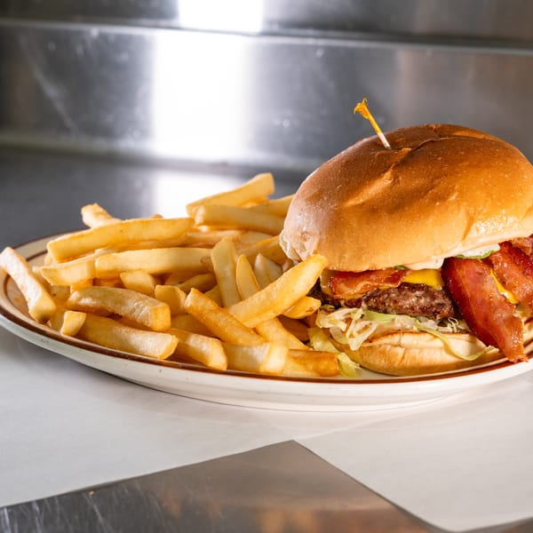 A bacon cheeseburger with lettuce and a side of golden french fries on a white plate.