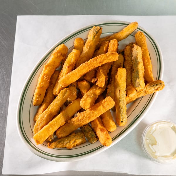 A white oval plate with green stripes holds a pile of golden-brown fried zucchini sticks and a side of ranch.