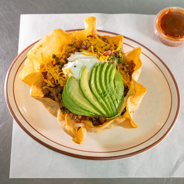 Taco salad in a crispy tortilla bowl, topped with ground beef, cheese, sour cream, and avocado slices.