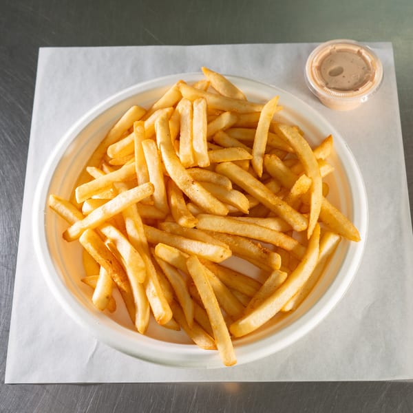 A white plate filled with golden french fries and a small container of dipping sauce.