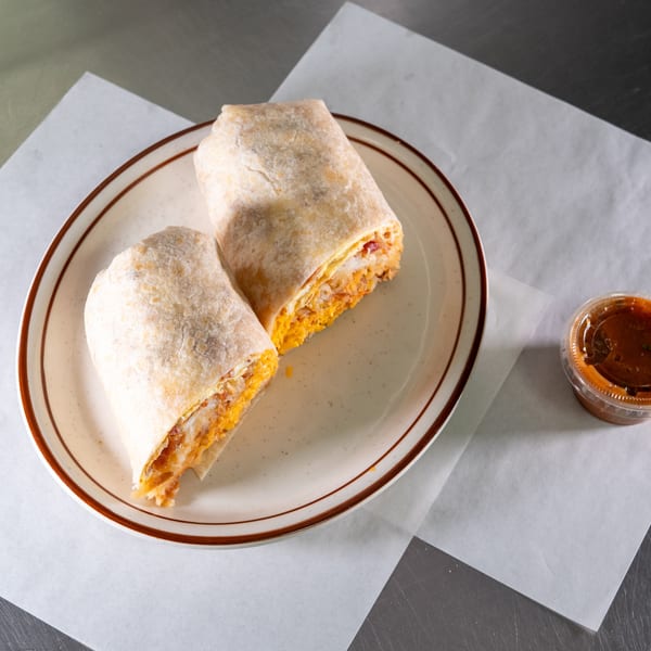 Two halves of a breakfast burrito, filled with eggs, cheese, and hash browns, on a plate with salsa.