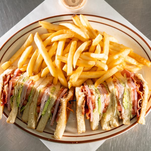 A club sandwich with bacon, ham, avocado, lettuce, and tomato, served with golden french fries.