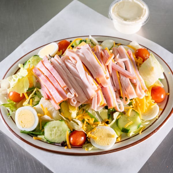 Chef salad with ham, cheese, hard-boiled eggs, tomatoes, and cucumbers on a white plate.