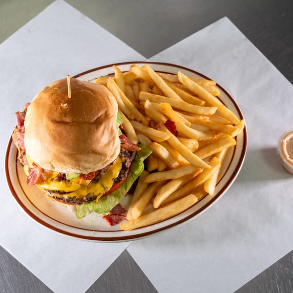 A double cheeseburger with bacon, lettuce, and tomato, served with a side of fries.