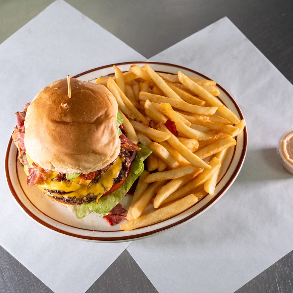 A double cheeseburger with bacon, lettuce, and tomato, served with a side of fries.